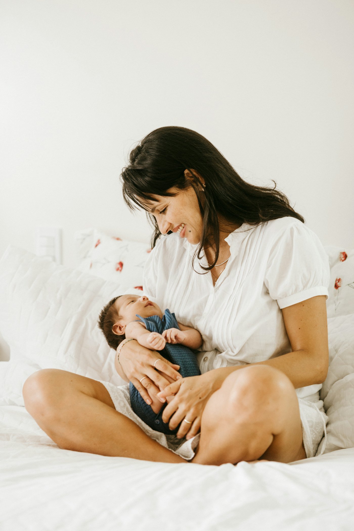 Mãe sentada na cama sorrindo para o bebê no colo